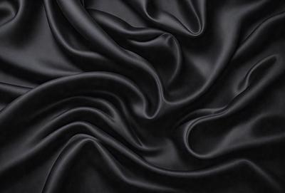 The primary subject of the image is a close-up of a black fabric, possibly a piece of clothing or a curtain. The setting is a dark background, which emphasizes the fabric's texture and pattern. The visual style appears to be a close-up or a detailed view of the fabric. The colors and mood of the image are predominantly dark, with the black fabric being the main focus.