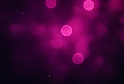 The primary subject of the image is a group of pink circles floating in a purple sky. The setting appears to be a nighttime scene with a dark background. The visual style of the image is a combination of digital art and illustration, creating a unique and captivating atmosphere. The dominant colors in the image are pink and purple, giving the scene a warm and dreamy mood.