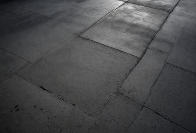 The primary subject of the image is a large, dark grey cement floor. The setting is a room with a concrete surface, which appears to be a part of a building. The visual style is a black and white photo, giving the image a classic and timeless appearance. The colors and mood of the image are predominantly dark and moody, with the grey cement floor serving as the main focal point.