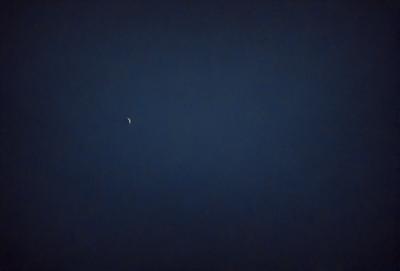 The primary subject of the image is a moon, which is visible in the dark sky. The setting is a night sky, with no other objects or landmarks visible. The visual style is a black and white photo, which adds a sense of timelessness and elegance to the scene. The colors and mood of the image are predominantly dark and moody, with the moon being the only source of light in the sky.