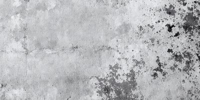 The primary subject of the image is a concrete wall with a dirty, worn-out appearance. The setting is an outdoor environment, with the wall being the main object of focus. The visual style is a photo, capturing the concrete wall in its natural state. The colors and mood of the image are predominantly gray and dull, reflecting the aged and worn-out nature of the wall.