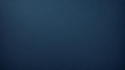 The primary subject of the image is a dark blue sky. The setting is a vast, open space with no visible landmarks or objects. The visual style is a natural, outdoor scene. The colors and mood are predominantly dark and moody, with the blue sky serving as the main focal point.