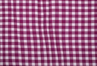 The primary subject of the image is a large, purple and white checkered cloth. The setting is a room with a checkered pattern on the wall. The visual style is a close-up of the checkered cloth, showcasing its intricate design. The colors and mood of the image are predominantly purple and white, creating a calm and elegant atmosphere.