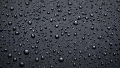 The primary subject of the image is a close-up of a black surface with numerous small bubbles on it. The setting appears to be a dark room, and the visual style is a close-up of the bubbles on the black surface. The colors in the image are predominantly black, and the overall atmosphere is somewhat moody and mysterious.