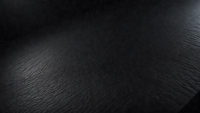 The primary subject of the image is a close-up of a black leather surface. The setting is a dark room, and the visual style is a photo. The dominant colors are black and the overall atmosphere is dark and moody.
