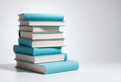 The primary subject of the image is a stack of books. The books are blue and white, and they are arranged in a pile. The setting is a white background, which provides a clean and minimalist look to the image. The visual style is a close-up of the books, showcasing their colors and textures. The overall atmosphere of the image is calm and organized, with the books neatly stacked on top of each other.
