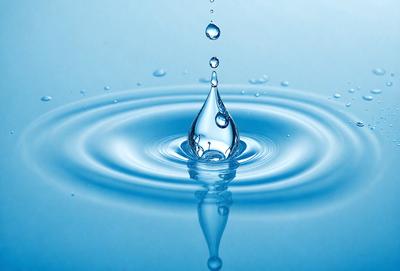 The primary subject of the image is a single drop of water, which is captured in mid-air. The setting is a blue background, which adds to the overall visual style. The image is a photo, showcasing the natural beauty of the water drop. The colors are predominantly blue, creating a calm and serene atmosphere.