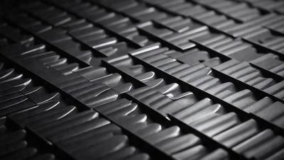 The primary subject of the image is a close-up of a patterned surface, which appears to be a black and grey metal. The setting is a dark room, and the visual style is a close-up of the patterned surface. The colors and mood of the image are predominantly dark and moody, with the black and grey metal creating a striking contrast against the dark background.