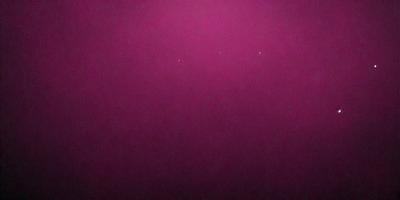 The primary subject of the image is a pink background. The setting is a dark, purple-colored space. The visual style is a close-up of the pink background, which creates a striking contrast with the darker surroundings. The colors and mood of the image are predominantly pink and dark, creating a moody and dramatic atmosphere.