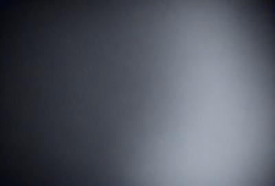 The primary subject of the image is a large, dark, and empty room. The setting is a dimly lit space with a grayish-blue color scheme. The visual style is a black and white photo, which adds a sense of depth and contrast to the scene. The overall atmosphere is one of emptiness and quietness, with no signs of life or activity.