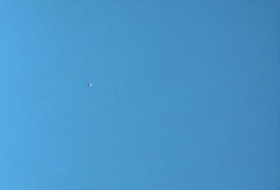 The primary subject of the image is a satellite in the sky. The setting is a clear blue sky, with no clouds or other obstructions visible. The visual style is a photo, capturing the satellite in its natural environment. The colors and mood of the image are predominantly blue, creating a calm and serene atmosphere.