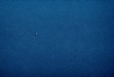 The primary subject of the image is a small, round, white object floating in a vast, dark blue sky. The setting is a vast, open space with no visible landmarks or other objects. The visual style is a realistic representation of the scene, with no indication of digital manipulation or artistic alteration. The colors and mood of the image are predominantly dark and moody, with the white object being the only bright spot in the otherwise dark and empty sky.
