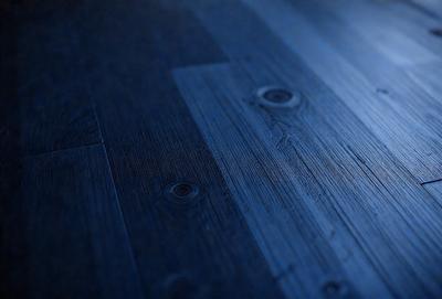 The primary subject of the image is a wooden floor. The setting is a room with a wooden floor, and the visual style is a photo. The colors and mood of the image are predominantly blue, creating a calm and serene atmosphere.