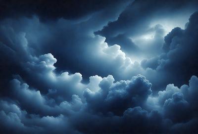 The primary subject of the image is a cloudy sky with dark clouds and a blue background. The setting is a cloudy day, and the visual style is a painting or drawing. The colors and mood of the image are dark and moody, with the clouds creating a dramatic atmosphere.