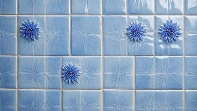 The primary subject of the image is a blue tile with a flower design on it. The setting is a bathroom, as indicated by the blue tiles. The visual style is a photo, capturing the intricate details of the tile. The dominant colors are blue and white, creating a calm and soothing atmosphere.