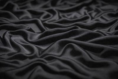 The primary subject of the image is a black fabric with a pattern of wrinkles and folds. The setting is a black background, and the visual style appears to be a close-up of the fabric. The colors and mood of the image are predominantly dark and moody, with the black fabric creating a dramatic and intense atmosphere.
