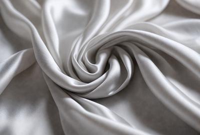 The primary subject of the image is a close-up of a white fabric, possibly a sheet or a curtain. The setting is a white background, which provides a clean and minimalistic appearance. The visual style is a close-up, focusing on the details of the fabric. The colors and mood of the image are predominantly white, giving it a clean and serene atmosphere.