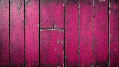 The primary subject of the image is a wooden surface with a pinkish hue. The setting appears to be a room with a wooden floor. The visual style of the image is a close-up of the wooden surface, which gives it a textured and rustic appearance. The dominant colors in the image are pink and brown, creating a warm and inviting atmosphere.