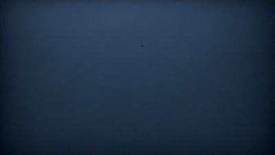 The primary subject of the image is a blue sky with a bird flying in it. The bird is located in the middle of the sky, and it appears to be flying towards the viewer. The setting is a vast, open sky, with no visible landmarks or objects. The visual style is a natural, outdoor scene, and the colors are predominantly blue, creating a calm and serene atmosphere.