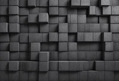 The primary subject of the image is a large, black brick wall. The setting is a dark room, and the visual style is a black and white photo. The dominant colors are black and white, creating a moody atmosphere.