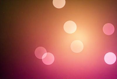 The primary subject of the image is a pink background with a pattern of circles. The circles are of various sizes and are scattered across the background. The setting appears to be a dark room, and the visual style is a combination of a photo and a digital art. The dominant colors in the image are pink and orange, creating a warm and inviting atmosphere.
