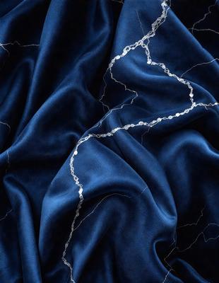The primary subject of the image is a blue fabric with a metallic texture. The setting is a dark background, which contrasts with the blue fabric. The visual style is a close-up of the fabric, showcasing its unique texture. The colors and mood of the image are predominantly dark and moody, with the blue fabric serving as the focal point.