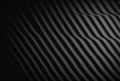 The primary subject of the image is a black and white striped pattern. The setting is a dark background, which creates a contrast with the pattern. The visual style is a black and white photo, giving it a classic and timeless appearance. The colors and mood of the image are predominantly dark and moody, with the contrasting light and dark stripes adding a sense of depth and complexity to the pattern.