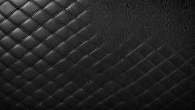 The primary subject of the image is a close-up of a black leather material. The setting is a black background, which creates a contrast with the leather material. The visual style is a close-up of the leather material, showcasing its texture and pattern. The colors and mood of the image are predominantly black, giving it a sleek and modern appearance.