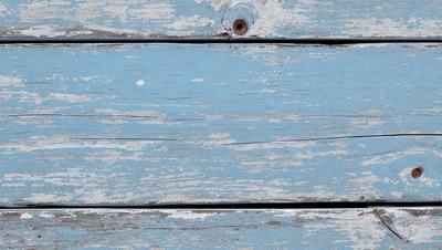 The primary subject of the image is a wooden plank with a blue background. The setting appears to be a wooden surface, possibly a table or a wall. The visual style of the image is a photo, capturing the wooden plank and its surroundings. The dominant colors in the image are blue and white, creating a calm and serene atmosphere.