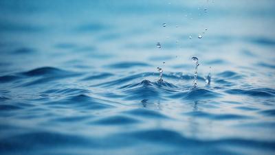 The primary subject of the image is a splash of water, which appears to be a close-up of a water drop. The setting is a blue ocean, and the visual style is a photo. The dominant colors are blue and white, creating a calm and serene atmosphere.