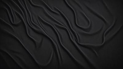 The primary subject of the image is a black fabric with a pattern of wrinkles and folds. The setting is a dark background, which emphasizes the fabric's texture and pattern. The visual style is a close-up of the fabric, showcasing its intricate details. The colors and mood of the image are predominantly dark, with the black fabric serving as the main focus.