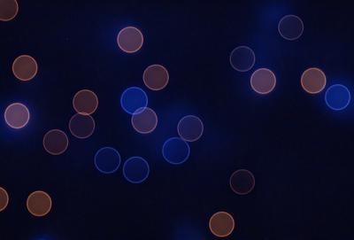 The primary subject of the image is a blue background with a pattern of glowing orange circles. The setting appears to be a dark, starry night, with the orange circles creating a sense of depth and contrast against the blue background. The visual style of the image is a combination of digital art and illustration, with the orange circles resembling a starry night sky. The colors and mood of the image are predominantly blue and orange, creating a serene and captivating atmosphere.