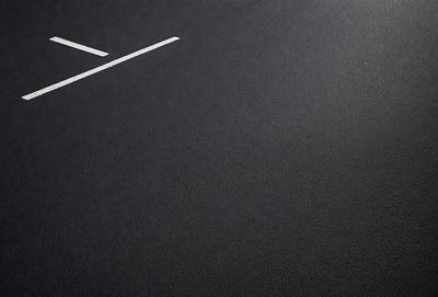 The primary subject of the image is a parking lot with a white line painted on it. The setting is a blacktop surface, and the visual style is a photo. The colors in the image are predominantly black and white, giving it a stark and minimalist appearance.
