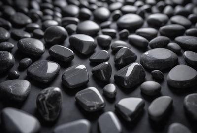The primary subject of the image is a collection of black rocks. The setting is a black background, which creates a striking contrast with the rocks. The visual style is a close-up of the rocks, showcasing their unique shapes and textures. The colors and mood of the image are predominantly dark, with the black rocks being the main focus.