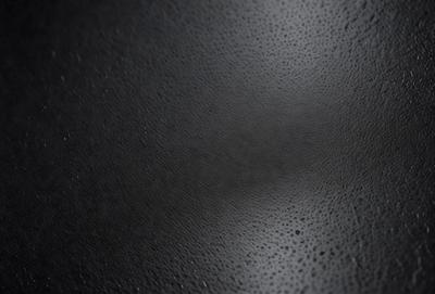 The primary subject of the image is a close-up of a black leather surface. The setting is a dark room, and the visual style appears to be a photo. The dominant colors are black and grey, creating a moody atmosphere.