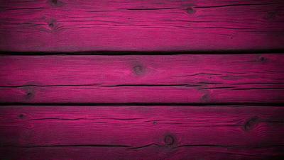 The primary subject of the image is a wooden wall with a pinkish hue. The setting is a room with a wooden floor. The visual style is a close-up of the wooden wall, showcasing its texture and color. The dominant colors are pink and brown, creating a warm and inviting atmosphere.