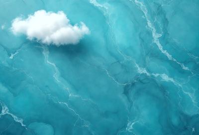 The primary subject of the image is a cloud floating in the sky. The setting is a blue ocean, creating a serene and calming atmosphere. The visual style is a photo, capturing the beauty of the cloud and the ocean. The dominant colors are blue and white, with the cloud being predominantly white and the ocean being a deep blue.