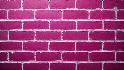 The primary subject of the image is a brick wall, which is the main object, scene, or focus of the image. The setting/background features a pink brick wall, which is the environment, backdrop, or surface visible in the image. The visual style of the image is a photo, as it is a real-life brick wall. The dominant colors in the image are pink, which gives the wall a warm and inviting atmosphere.