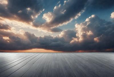 The primary subject of the image is a wooden floor with a cloudy sky in the background. The setting appears to be a rooftop, as the sky is visible above the wooden surface. The visual style of the image is a photo, capturing the natural light and cloudy atmosphere. The colors in the image are predominantly shades of gray and white, creating a calm and serene mood.
