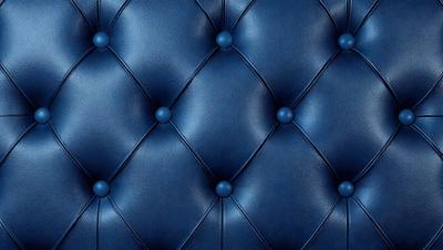 The primary subject of the image is a blue leather couch with a patterned design. The setting is a room with a blue background, and the visual style is a close-up of the couch. The colors and mood of the image are predominantly blue, creating a calm and relaxing atmosphere.