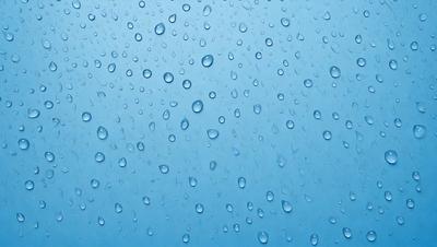 The primary subject of the image is a close-up of water droplets on a blue surface. The setting is a clear blue sky, and the visual style is a photo. The colors are predominantly blue, and the overall atmosphere is serene and calming.
