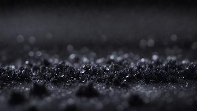 The primary subject of the image is a black surface with a pattern of small black dots. The setting is a dark room, and the visual style appears to be a close-up of the black surface. The colors and mood of the image are predominantly dark and moody, with the black dots creating a sense of depth and intrigue.