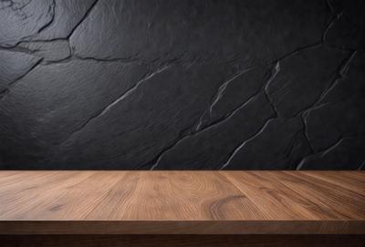 The primary subject of the image is a wooden table with a black marble top. The table is placed against a black stone wall, which serves as the setting and background of the scene. The visual style of the image is a photo, capturing the details of the table and the wall. The colors and mood of the image are dark and moody, with the black marble top and the black stone wall creating a dramatic and striking contrast.