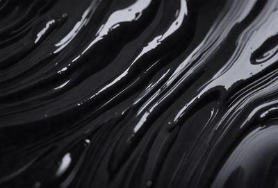 The primary subject of the image is a close-up of a black, swirling liquid, possibly a dark substance or a patterned surface. The setting is a black background, which contrasts with the swirling liquid. The visual style appears to be a close-up of a pattern or a texture, creating a moody and intriguing atmosphere.