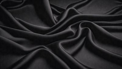 The primary subject of the image is a black fabric, which is the main object, scene, or focus of the image. The setting/background consists of a dark background, and the visual style is a close-up of the fabric. The colors and mood of the image are predominantly black, creating a moody and dramatic atmosphere.