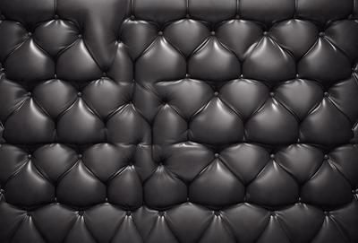 The primary subject of the image is a black leather couch. The setting is a black background, which creates a striking contrast with the couch. The visual style is a close-up of the couch, showcasing its texture and details. The colors and mood of the image are predominantly black, giving it a sleek and modern appearance.