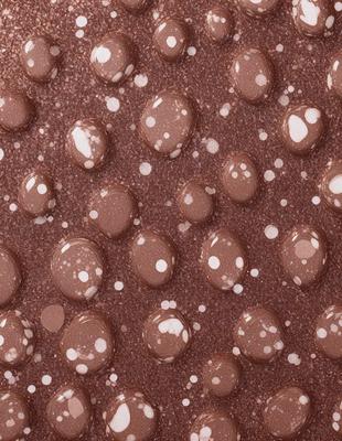 The primary subject of the image is a close-up of a chocolate-covered candy, which is the main focus of the image. The setting is a brown surface, possibly a table or a counter, with a pattern of white dots on it. The visual style of the image is a close-up of the candy, showcasing its texture and details. The colors in the image are predominantly brown and white, creating a warm and inviting atmosphere.