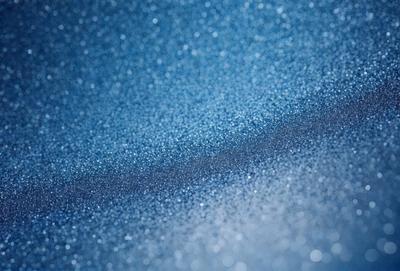 The primary subject of the image is a blue surface with a pattern of glittering, shiny, and sparkling blue dots. The setting appears to be a dark room, and the visual style is a close-up of the blue surface. The colors and mood of the image are predominantly blue, with a sense of depth and shine from the glittering dots.