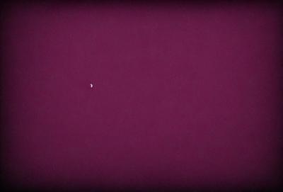 The image features a purple background with a small white moon in the upper left corner. The moon is the primary subject of the image, and it stands out against the dark purple sky. The setting appears to be a nighttime scene, with the moon being the main focus of the visual style. The colors and mood of the image are predominantly dark and moody, with the purple background providing a contrasting backdrop for the white moon.