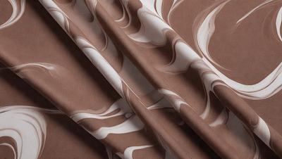 The primary subject of the image is a brown and white patterned fabric. The setting is a room with a wall, and the visual style is a close-up of the fabric. The colors and mood of the image are warm and inviting, with the brown and white pattern creating a sense of texture and depth.